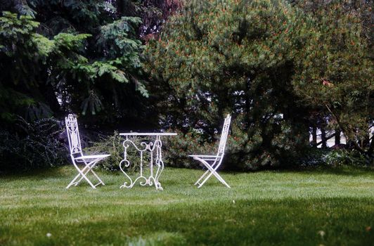 White garden furniture on the lawn. A chair and a table in the garden. Equipped backyard.