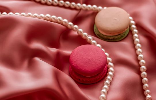 Girly, bakery and branding concept - Sweet macaroons and pearls jewellery on silk background, parisian chic jewelry, French dessert food and cake macaron for luxury confectionery brand, holiday gift