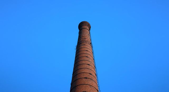 tall chimney old red bricks in an old factory. smoke stack An old brick chimney against a blue sky.