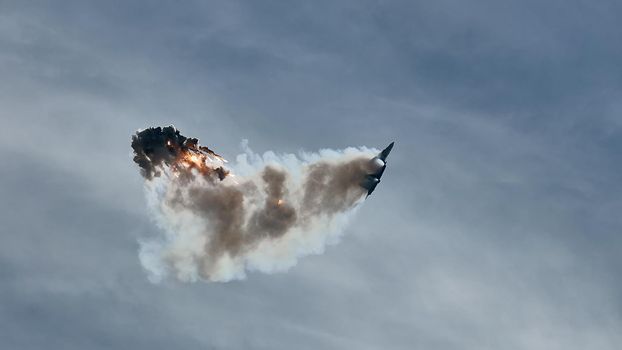 Aircraft fighter flies and shoots heat guns in the blue sky. Fighter shoots off heat traps during the maneuver. A fighter during a demonstration aerobatics.