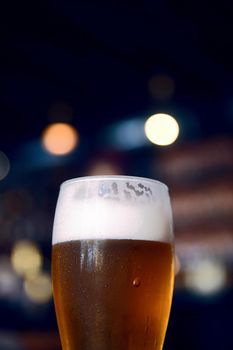 Glass of beer on a table in a bar on blurred bokeh background.