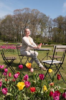 young woman in a beige jumper takes a selfie in the park with blooming tulips. High quality photo
