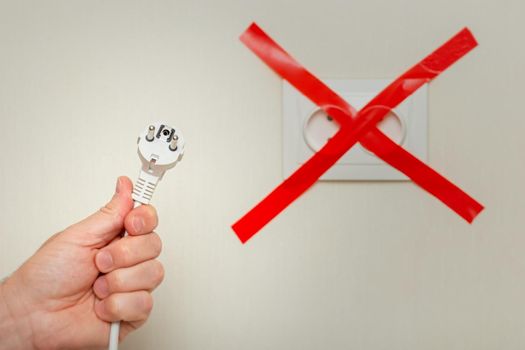 A mans hand holds a white cord with a plug near an electrical outlet, tied with a red ribbon crosswise. The concept of the energy crisis in Europe