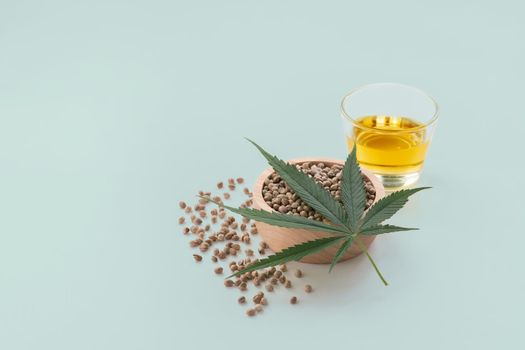 CBD oil, THC tinture in glass bowl and bottle with dropper lid and hemp leaf on empty background with a pile of dry hemp seeds surrounded in minimalism. Legalized marijuana concept.