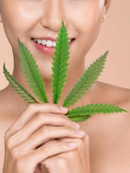 Closeup portrait of young ardent girl with healthy fresh skin holding green hemp leaf. Combination of beauty and cannabis concept.