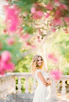 Smiling bride under a tree blooming with pink flowers in the garden. High quality photo