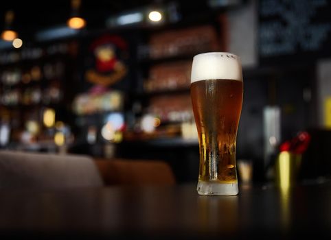 Glass of beer on a table in a bar on blurred bokeh background.