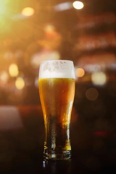 Glass of beer on a table in a bar on blurred bokeh background.