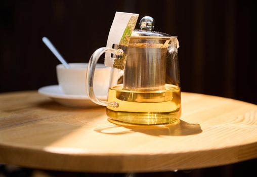 Front shot of a teapot with healthy antioxidant herbal, green tea on a wooden table. Sunlight falling on the healing drink. Food and drink consumerism. Detox therapy. Recreation.