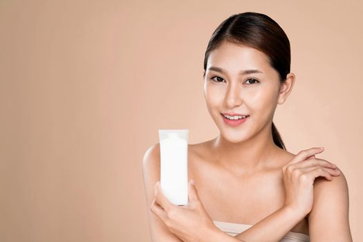 Ardent woman smiling holding mockup product for advertising text place, light grey background. Concept of healthcare for skin, beauty care product for advertising.