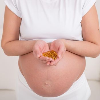 A pregnant woman with a bare belly holds a handful of vitamins. Transparent golden pills. Vitamin D for the expectant mother
