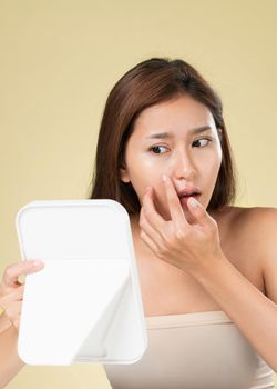 Portrait of young ardent asian woman looking in the mirror worry about pimple on her face. Beauty care for skin problem, acne treatment concept.