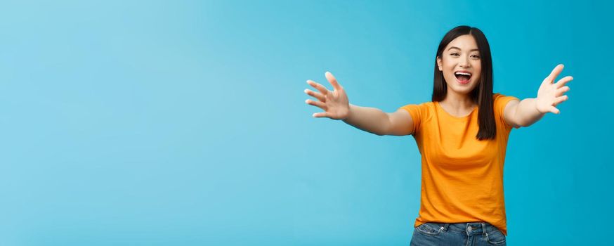 Come closer let me hug you. Cheerful lovely asian brunette girl stretch hands forward wanna cuddle, embracing friend smiling broadly inviting dear guests welcoming, stand blue background.