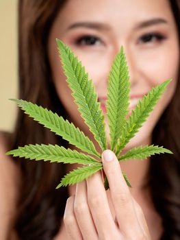 Closeup portrait of young ardent girl with healthy fresh skin holding green hemp leaf. Combination of beauty and cannabis concept.