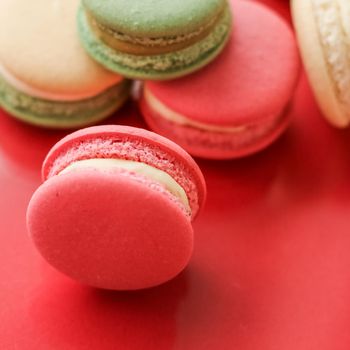 Pastry, bakery and branding concept - French macaroons on fruity red background, parisian chic cafe dessert, sweet food and cake macaron for luxury confectionery brand, holiday backdrop design