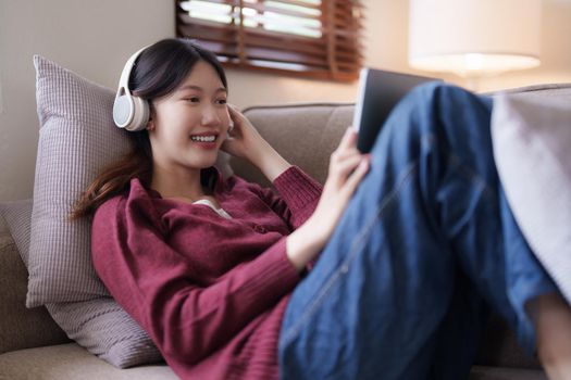 Attractive smiling young woman using tablet and listen music on sofa at home. lifestyle concept.