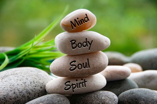 Mind, Body, Soul and Spirit words engraved on zen stones with blurred nature background. Copy space and zen concept.