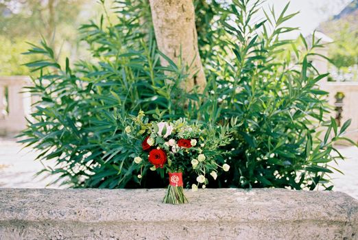 Bouquet of flowers stands on a stone balustrade against the background of a green bush. High quality photo