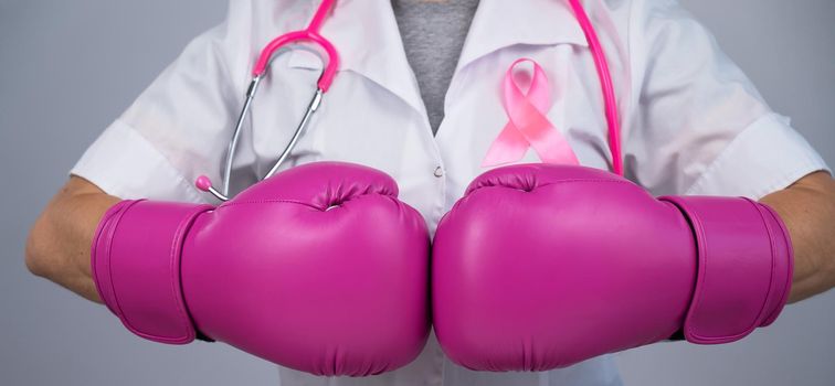 Faceless female doctor in pink boxing gloves with a pink ribbon on a gray background. Fight against breast cancer