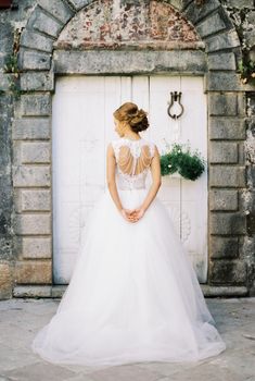 Bride stands in front of the white wooden door of an old stone building. High quality photo