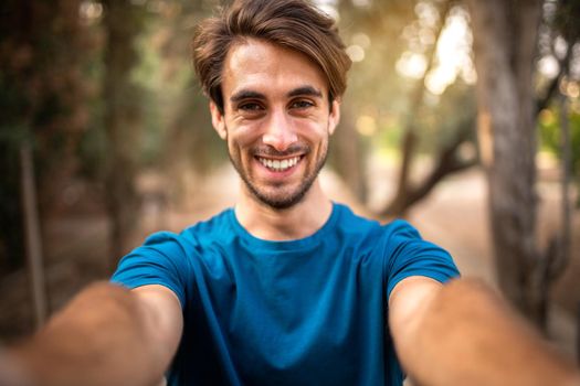 Young smiling caucasian man taking selfie in the forest looking at camera. Technology, lifestyle and people concepts.