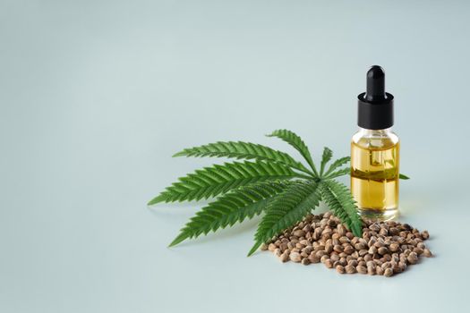 Legalized marijuana concept features with CBD oil extract from marihuana in glass bottle with dropper lid, piles of hemp seeds on empty background. Marijuana products for copyspace and advertising.