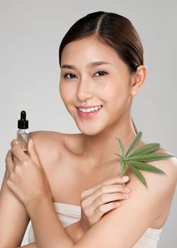 Closeup young ardent woman with healthy fresh skin holding green hemp leaf and cbd oil. Combination of beauty and cannabis concept.