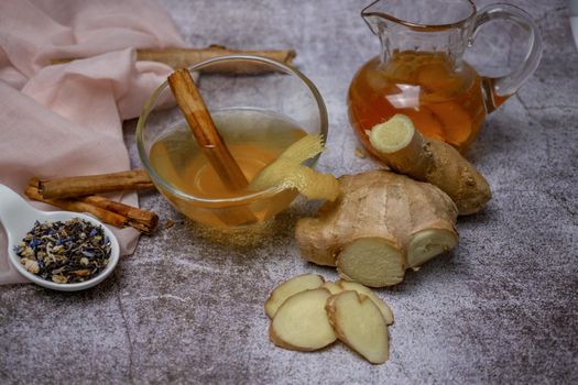 preparation of a ginger and cinnamon infusion with fresh produce natural roots and cinnamon stick served in a pitcher and a cup