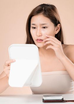 Portrait of young ardent asian woman looking in the mirror worry about pimple on her face. Beauty care for skin problem, acne treatment concept.