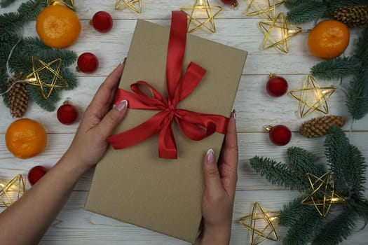 A woman's hand holds a gift in a craft package with a red satin bow. High quality photo