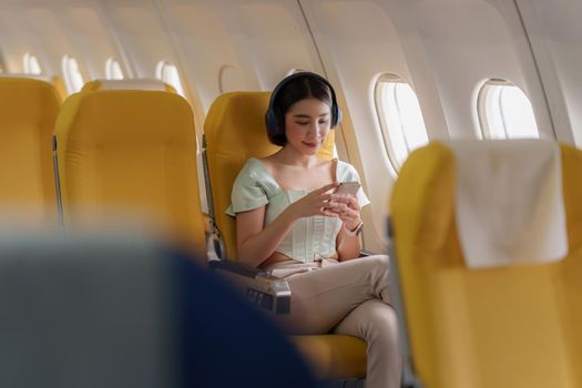 Young asian woman using smartphone connected to wifi internet during flight on board. Travel concept.