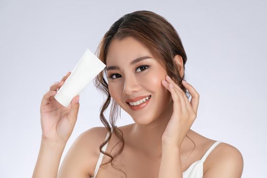 Gorgeous woman with makeup smiling holding mockup product for advertising text place, light grey background. Advertising concept for skin healthcare and beauty care products.