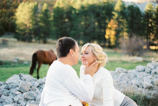 Man touches woman face with his hand while sitting on the edge of the forest. High quality photo