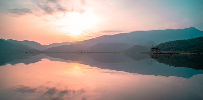 Panorama scenic of mountain lake with perfect reflection at sunrise. beautiful mountain range landscape with pink pastel sky with hills on background and reflected in water. Nature lake landscape