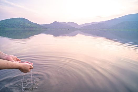 Woman taking clear water by hands on nature lake mountain background