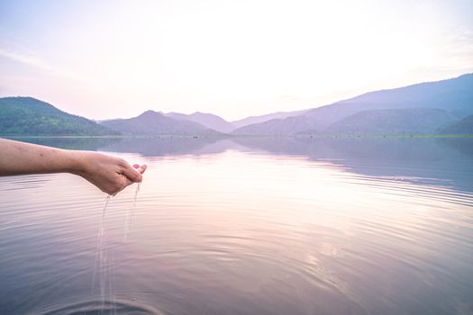 Woman taking clear water by hands on nature lake mountain background