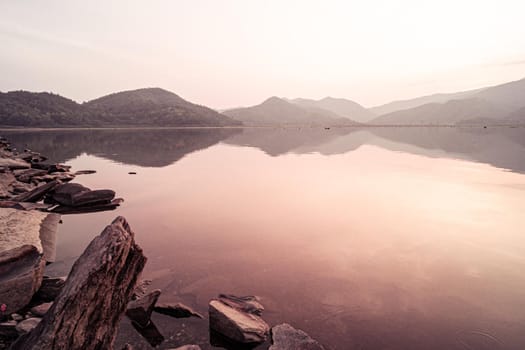 Panorama scenic of mountain lake with perfect reflection at sunrise. beautiful mountain range landscape with pink pastel sky with hills on background and reflected in water. Nature lake landscape