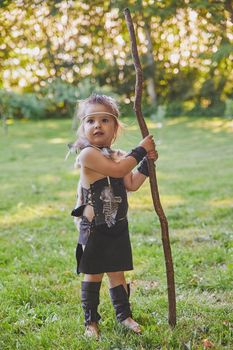 Cute baby dressed in the clothes of primitive people with combat staff.