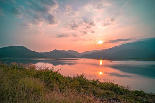 Panorama scenic of mountain lake with perfect reflection at sunrise. beautiful mountain range landscape with pink pastel sky with hills on background and reflected in water. Nature lake landscape