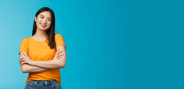 Cheerful friendly asian woman with dark short haircut smiling broadly enthusiastic conversation, talking you casually, cross arms chest confident pose, laughing carefree, stand blue background.