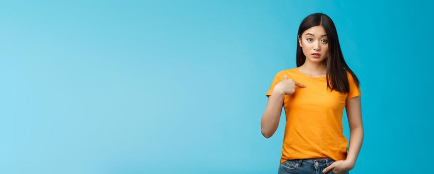 Surprised cute asian urban female student pointing herself look questioned, full disbelief cannot understand, hear own name, look clueless, unsure standing blue background astonished.