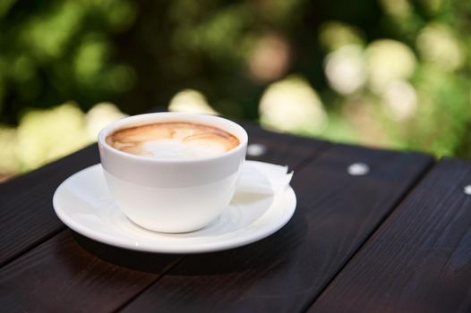 Frothy cappuccino coffee with foam in a beautiful white cup on the wooden table. Favorite cup of coffee concept. Copy advertising text