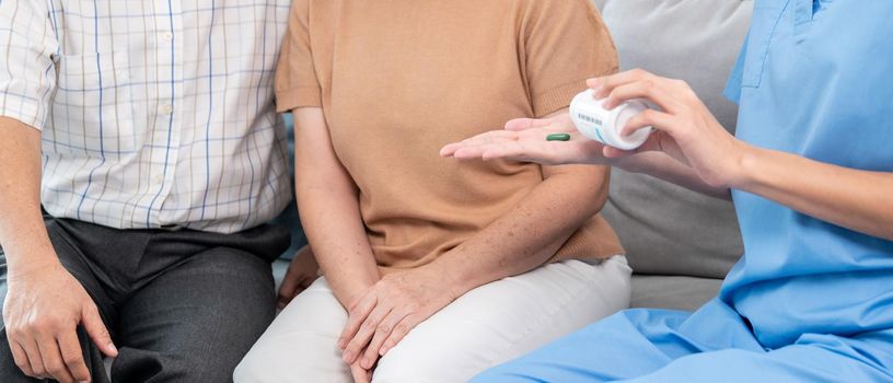 Contented senior woman sit along side with her husband, taking medicines while her caregiver advising her medication. Medication for seniors, nursing house, healthcare at home.