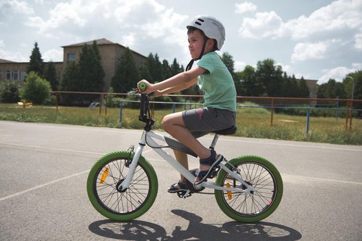 Active sporty Caucasian schoolboy, wearing sports helmet cycling on a bicycle on the asphalt road in urban environment. Active lifestyle and sport concept