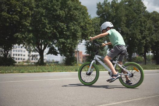 A school-age boy learns extreme tricks and extreme cycling in the city. Sporty child in protective gear riding a bicycle, cycling on the asphalt road outdoors. Sport. Active, healthy lifestyle concept