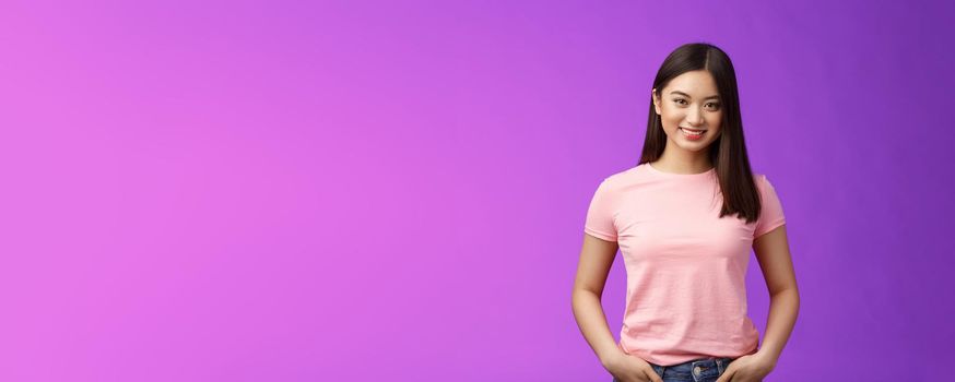 Cute tender feminine asian woman dark short haircut, stand pink t-shirt encouraged, hold hands jeans pockets, smiling joyfully, keep interesting conversation, stand purple background upbeat.