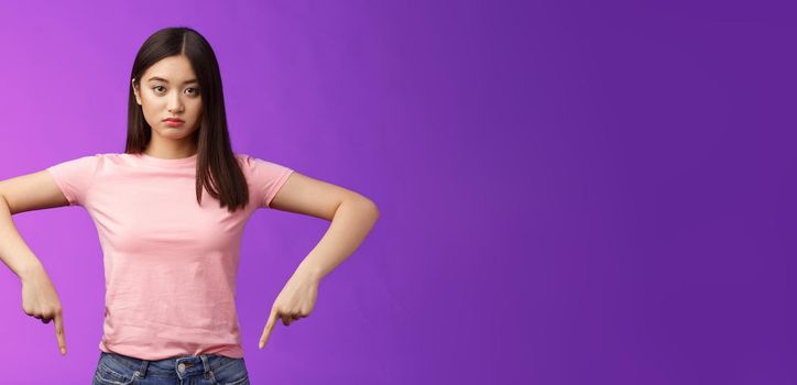 Serious-looking upset insecure asian female fighting stop cruel animal behaviour, pointing fingers down disappointed, look camera sincere fed up, standing depressed unsatisfied, purple background.