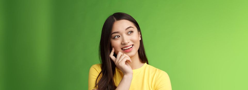 Close-up dreamy intrigued creative asian brunette woman imaging summer vacation trip, picturing perfect holiday, standing thoughtful, touch cheek, thinking look up, stand green background.