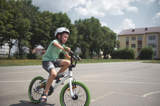 Active sporty 10 years old European boy in sports helmet confidently riding bike. Caucasian school age child cycling on the city asphalt road. Healthy lifestyle. Physical exercises. Motion. Extreme