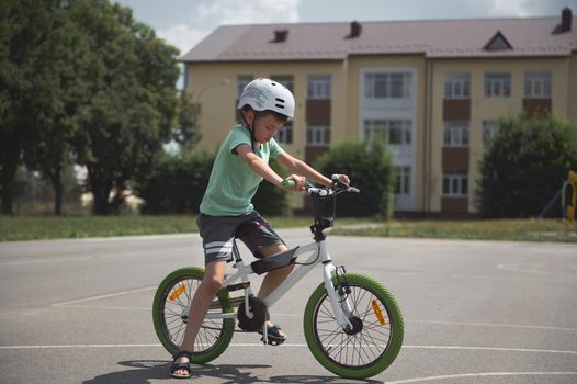 Side view school-age boy learns extreme tricks and cycling in the city. Sporty child in protective gear riding a bicycle, cycling on the asphalt road outdoors. Sport. Active, healthy lifestyle concept